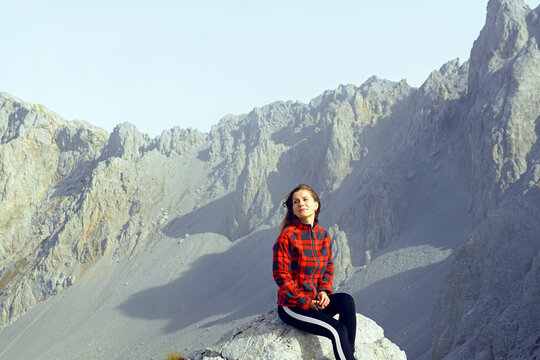Enjoying the beauty of nature: portrait of a young smiling woman sitting on the top against the backdrop of a picturesque mountain. Female tourist on a hiking holiday in Komovi Nature Park, Montenegro