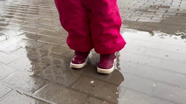 Children's feet stomp in a puddle, close-up, girl walks in a puddle in the rain, autumn, spring.