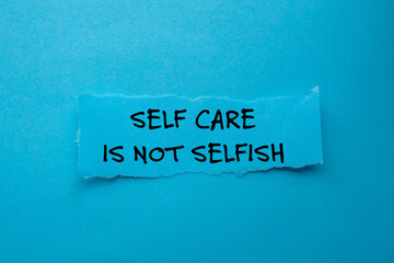 Self care is not selfish message written on ripped torn paper piece on blue background. Conceptual...