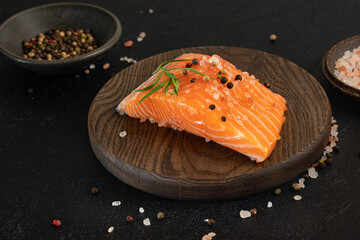 Salmon fillet seasoned with rosemary, salt, peppercorns, lying on wooden cutting board, ready for...
