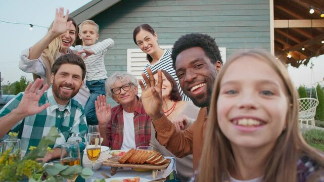Group of people enjoying eating food outside. Family gathering together on weekend while visiting their parents. Everyone waving and smiling. Staying in village during time off work.
