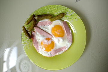 Delicious Breakfast of Fried Eggs with Ham and Pickles on a Green Plate. Home.Cooked Meal with Rustic Appeal