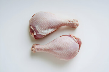 Two raw chicken drumsticks on a plain white background