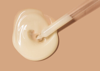 Cosmetic beauty swatch sample. Liquid opaque yellow milky ampoule or serum on beige isolated background