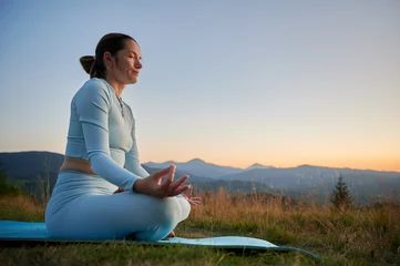 Fototapete Woman practicing yoga outdoors in the mountains in a serene, natural setting. Female doing yoga exercise and meditating during sunset in the evening. © anatoliy_gleb