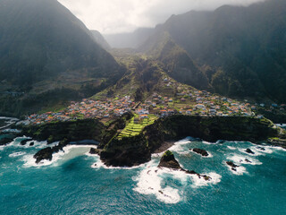 Aerial view of Seixal, Madeira, showcasing coastal cliffs, green terraces, colorful houses, and the blue ocean waves crashing against the shore.