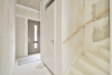 A sleek, modern interior featuring a white staircase and a contemporary door design, set against minimalistic walls. The space is bright and inviting.