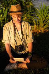 Photographer smiling and looking at printed photo while sitting on grass in park