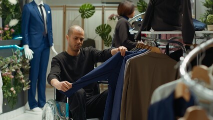 Male wheelchair user searching for new trendy clothes at a disability friendly boutique, enjoying...