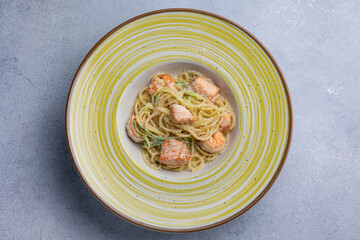 Spaghetti with salmon and herbs in a bowl on the table.