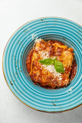 Italian lasagna on a blue plate with a fork and basil leaf