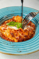 Italian lasagna on a blue plate with a fork and basil leaf