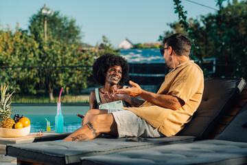 Interracial couple relaxing and chatting by the pool on a sunny day