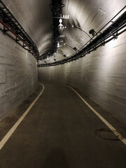 A deserted tunnel stretches ahead, featuring a distinctive white line running alongside it, creating a stark contrast against the grey and dark surroundings, bathed in monochrome tones