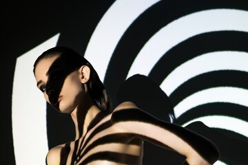Model poses against abstract light patterns with striking shadows in studio