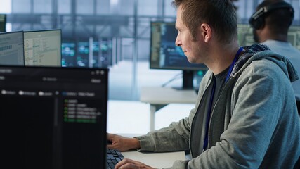 IT technician looking at PC screen, working in network security data center, ensuring optimal...