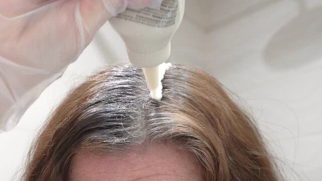 Coloring of gray hair.A woman applies hair dye to gray roots using a special applicator. The process of home coloring helps to return a rich color and hide gray hair.