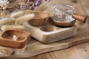 Close up of wooden items laid on a wooden table. There are dried flowers on the table. The light is bright. The atmosphere is peaceful. This scene  evoke something healthy and natural. Still life