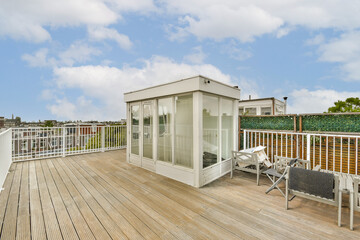 Spacious rooftop terrace featuring a contemporary glass pavilion, wooden deck, and seating area, offering a vibrant view of the surrounding cityscape.