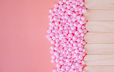 A close-up of depilatory wax granules and wooden wax sticks, essential tools for professional and...