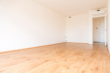 Bright empty apartment room with wooden flooring, white walls, and air conditioning unit. Spacious modern real estate interior, ideal for property sale or rent. No people, copy space.