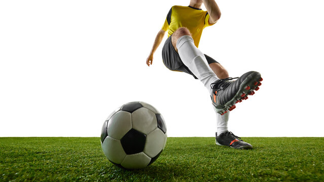 Low angle, close-up image of young man, soccer player striking ball with powerful kick, intense action on green field. Concept of sport, action, competition, game, active lifestyle. Ads