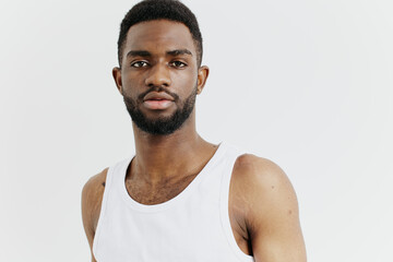 Confident black man in white tank top standing with hands on hips against white background