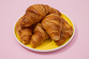 Croissants piled on a yellow plate on a minimalist pastel pink background, puff pastry bakery piece
