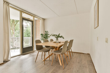 A stylish dining area featuring a wooden table and gray chairs, bathed in soft natural light from large windows with a serene outdoor view.