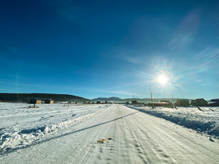 A serene snowy road extends ahead, with golden sunlight filtering through the clouds, creating a stunning contrast with the bright, pristine snowcovered landscape of winter