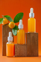 Three bottles with Serum with vitamin C in cosmetic transparent vials with dropper lid. Unmarked container on wooden podium for product presentation.