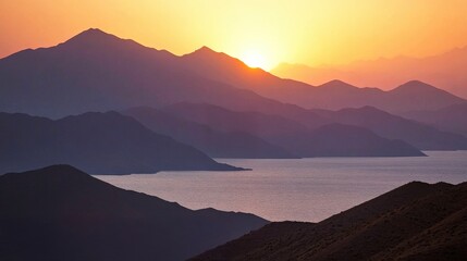 Obraz premium A serene sunset over mountains, casting warm hues across the water and creating a tranquil landscape.
