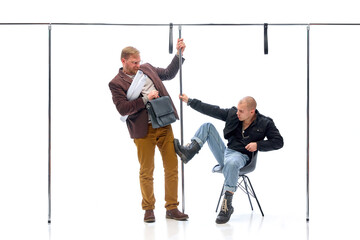 Businessman holding onto rail while aggressive young man in black boots grabs pole in defensive...