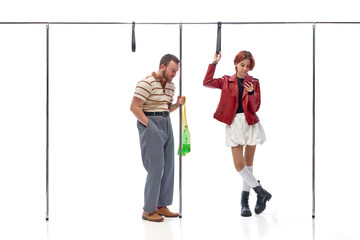 Young man holding shopping bag and woman in stylish outfit looking at phone while commuting against...