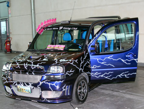 Rimini, Italy : 2019 03 29 Rimini Tuning free auto meeting Unique Fiat Doblo with a custom paint job featuring lightning bolt designs, showcased with an open door at an indoor event, 