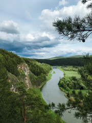 In a serene and picturesque valley, a winding river flows gently, embraced by vibrant, lush trees and greenery, all beneath a moody, cloudladen sky that speaks of natures tranquil beauty