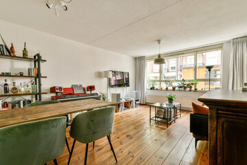 A stylish living room featuring wooden flooring, a modern dining area, and abundant natural light from large windows, creating a warm and inviting atmosphere.