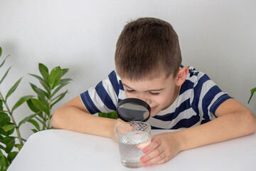 boy examines water in a glass with a magnifying glass. Selective focus