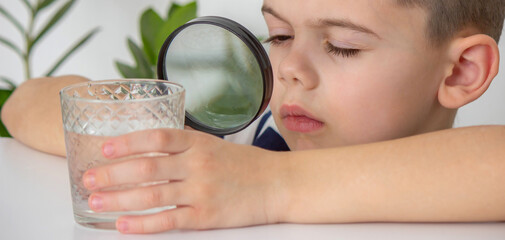 boy examines water in a glass with a magnifying glass. Selective focus