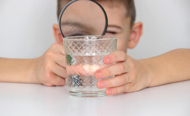 boy examines water in a glass with a magnifying glass. Selective focus
