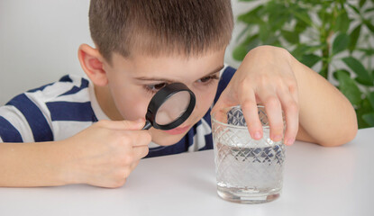 boy examines water in a glass with a magnifying glass. Selective focus