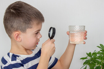 boy examines water in a glass with a magnifying glass. Selective focus