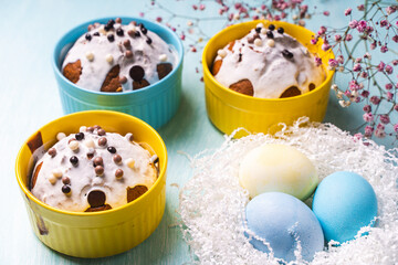 Delicious Easter cupcakes and eggs on a light blue background with flowers. Easter cakes with glaze in bright baking molds of yellow and sky color.