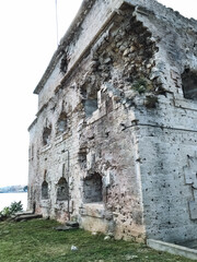 A large, imposing brick building that is characterized by an abundance of windows is perched majestically atop a gently sloping grassy hill, providing a picturesque view