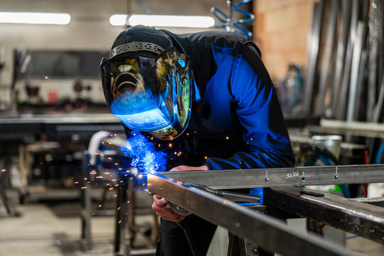 Dans un atelier de m&eacute;tallerie, un homme qui est en train de couper des barres de m&eacute;tal. L'homme porte un casque sur la t&ecirc;te. L'art et la pr&eacute;cision des m&eacute;talliers dans leur environnement de travail.