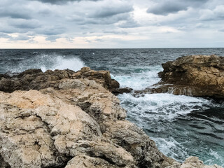 On a cloudy day, a rugged and rocky shoreline is revealed, with powerful waves crashing forcefully against the jagged rocks, creating a stunning and dramatic scene of natures beauty
