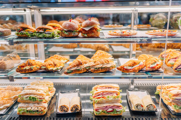A display case filled with a variety of fresh sandwiches, croissants, wraps, and burgers in a bakery or café, ready for customers to buy..