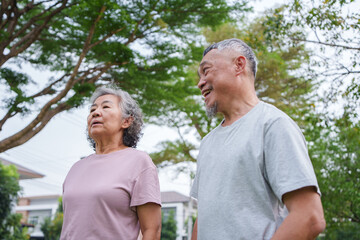 Obraz premium Smiling Asian Senior man and woman share a joyful moment while walking and breathing exercise in a vibrant park filled with trees and greenery.