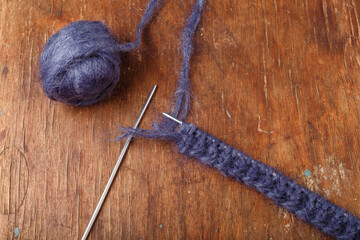Knitting needles and dark blue mohair yarn ball on old wooden table background. Starting a knit garment