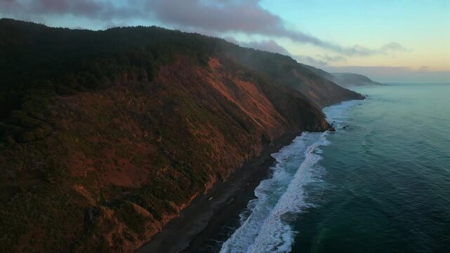 Northern California waves crashing bluffs cliffside mountain rocky rugged remote coastline aerial drone USAL Beach Campground sunset Sinkyone Wilderness surf swell black sand static shot